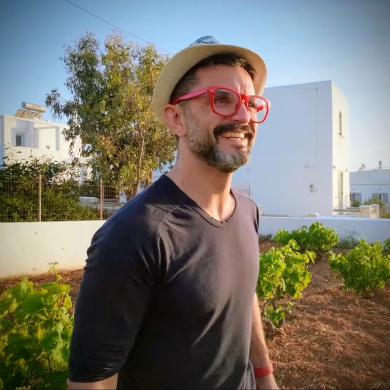 marc scheff standing in a dirt field wearing a white hat and red glasses smiling